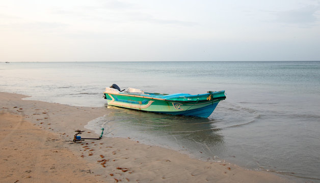 Small fishing boat anchored on Nilaveli beach at sunset in Sri Lanka Asia