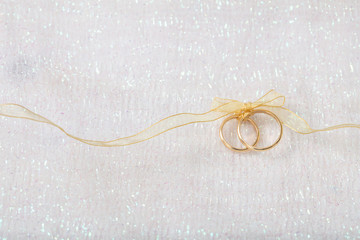 Two golden wedding rings tied with a golden ribbon on white shiny background