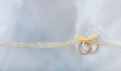 Two golden wedding rings tied with a golden ribbon on silver shiny background