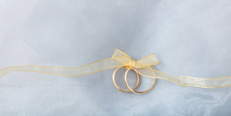 Two golden wedding rings tied with a golden ribbon on silver shiny background