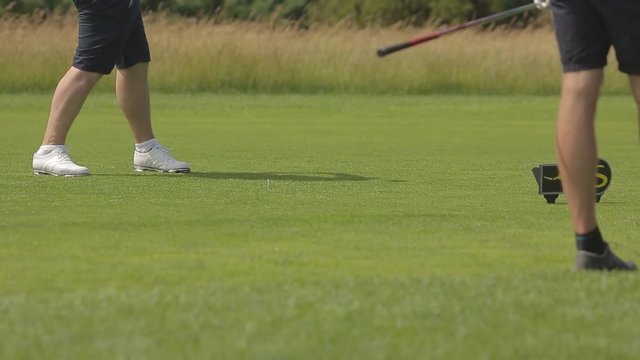 Adult man hits a golf ball with a one iron driver, shot from the legs down