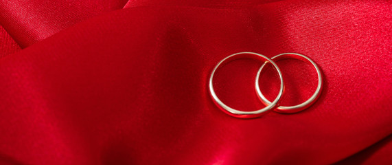 Two golden wedding rings on red satin background, banner, copy space