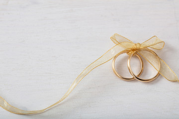 Two golden wedding rings tied with a golden ribbon on white wooden background