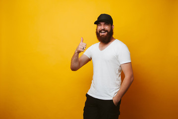 Happy young bearded man in white t-shirt showing thumbs up over yellow backgorund