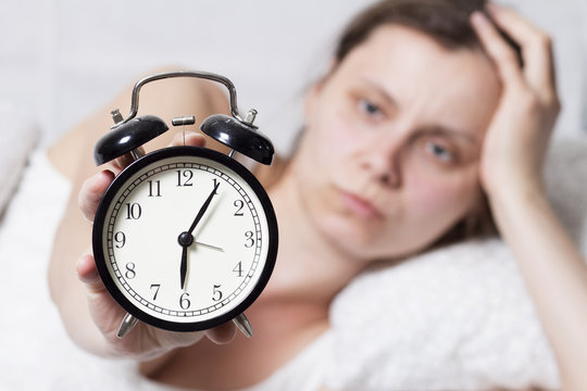 Dissatisfied sleepy woman holding a ringing alarm clock at 6 am.