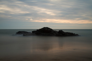 Fototapeta na wymiar Long exposure of a rock in the sea at sunset 
