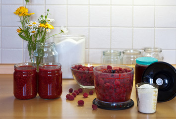 Crushing ripe raspberries in a blender with sugar, glass jars with ready-made homemade jam on the kitchen table. Seasonal preparation of vitamin products for future use