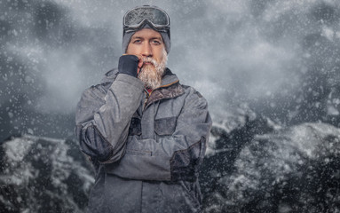 Portrait of a redhead snowboarder with a full beard in a winter hat and protective glasses dressed...
