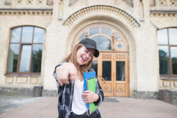 Portrait of a happy student with books and notebooks in the hands of the university building background. Stylish happy girl rejoices at campus. Student Concept