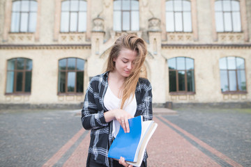 Portrait of an attractive student in a stylish casual dress with books and notebooks in his hands against the background of a university building. Cute girl student pose in. campus