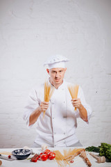 Male chef in restaurant kitchen is garnishing and preparing pasta dish. Italian cuisine. Paste. White chef uniform. Pasta spaghetti.