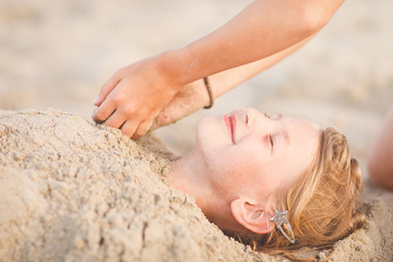 Two hands covering young girl in the sand at the beach