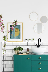Poster next to mirrors above green cabinet in bathroom interior with pink plant. Real photo