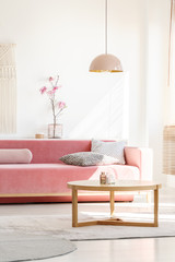 Retro style, millennial pink pendant lamp above a simple, wooden coffee table in a sunny, white...
