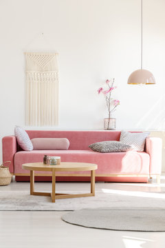Soft, warm living room interior with a cozy, velvet sofa, millennial pink decorations and a beige macrame on a white wall
