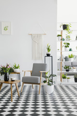 Checkered floor in a retro living room interior with white walls, plants, armchair and coffee table. Real photo