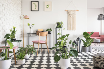 Botanical living room interior with checkered floor, chair and desk, graphics and decorations on the wall. Real photo