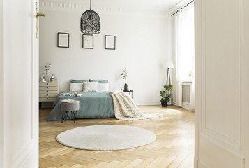 White round rug in spacious bedroom interior with green bed under lamp and posters. Real photo