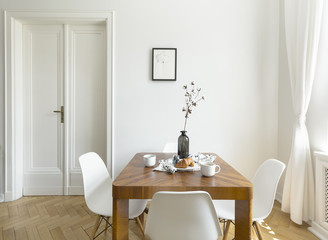 White chairs at wooden table in minimal dining room interior with door and poster. Real photo