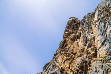 Big mountain cliff under cloudy sky close-up. Beautiful rocky gray textured background with vegetation. Majestic nature.