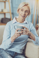 Warm atmosphere. Cheerful female person keeping smile on her face while going to drink tea