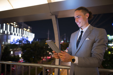 Fototapeta premium Young Handsome Businessman Outdoors At Night Using Digital Tablet