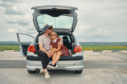 Happy couple have good time together while sitting in car trunk