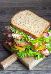 Two sandwiches with green salad, grilled turkey, bacon and vegetables on a wooden cutting board. Lunch concept.