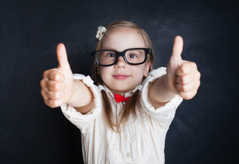 Smart Child Little Girl with Thumb Up Having Fun in Classroom on Chalk Board Background. Back to...