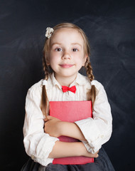 Сhild girl in school uniform clothes with book on chalk board background (child 5-6 years old)....