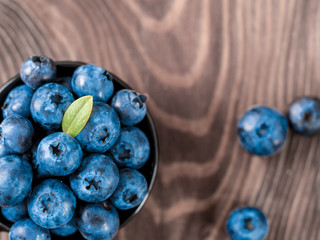 Blueberries in small black bowl on brown wooden tabletop. Top view of blueberry with copy space for text. Flat lay.