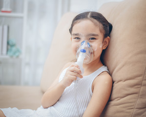 Cute Asian child  patient inhalation therapy by the mask of inhaler with soft stream smoke from bronchodilator.