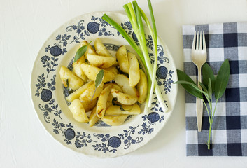 Young fried potatoes with onions and sage in a light plate on a light table.