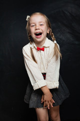Happy child girl in school uniform having fun and laughing on chalk board background. Back to...
