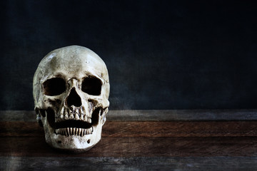 Halloween human skull on an old wooden table in front of black background with free space for text.