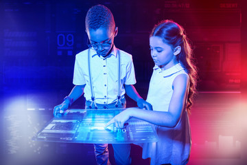 Transparent device. Careful thoughtful boy holding a futuristic transparent tablet and a curious girl pointing to the screen of it
