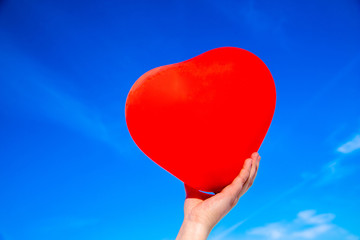 The girl holds the ball in the form of a heart against the blue sky 