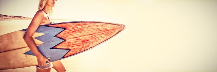 Woman carrying surfboard at beach during sunny day