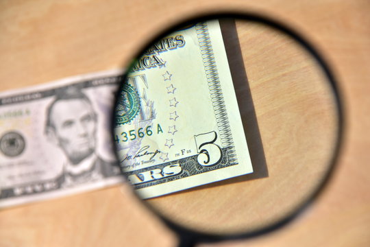 I look at a 5 dollar bill under a magnifying glass. The concept of verification for authenticity, bribery, money laundering, illegal income