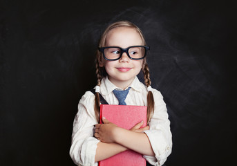 Little girl with red book on empty chalkboard background with copy space. Back to school, reading...