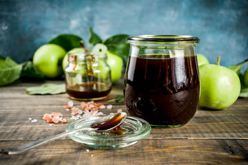 Home cooked dark salted classic caramel sauce, with green apples, wooden and dark blue background,