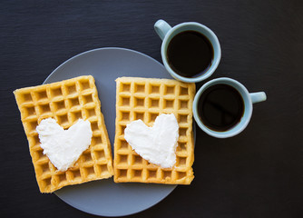 Delicious Belgian waffles with cream on a black background and two cups of coffee