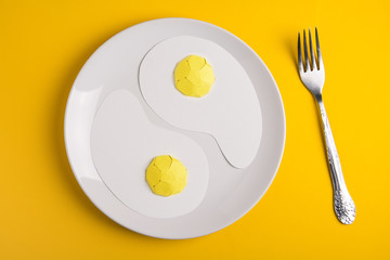 Top view of white plate with paper fried eggs on yellow paper background. Good morning or food art