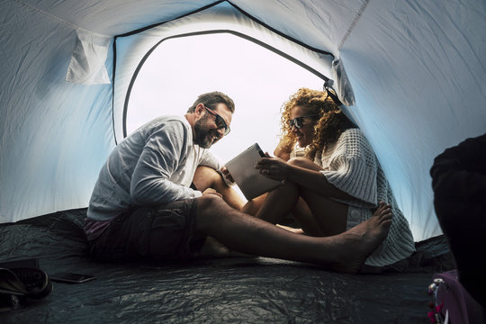 Happy Young Middle Age Couple Married And In Relationship Enjoy The Camping Inside The Tent And Use Tablet Internet Technology. Love And Friendship For Alternative Traveler. Wanderlust And Enjoy