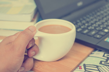 Cup of coffee on the wooden laptop, books on the bed.
