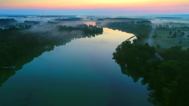 Misty predawn aerial flyover of scenic winding river. 
