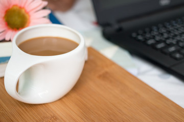 Cup of coffee on the wooden laptop, books on the bed.