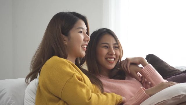 Happy Asian lesbian lgbt couple enjoy entertainment in living room. Beautiful women lying on a sofa with remote control and watching video and movie on television at home.