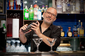 Professional bartender man holding in hands a shaker with a fresh delicious cocktail. Bartender shaking a cocktail shaker as she stands behind the bar mixing a drink for a client. Close-up.