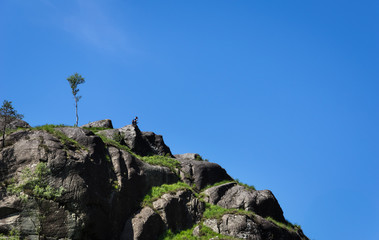 Man Sitting Alone on the Rocks Cliff with Isolated Tree Blue Sky in Summer Scotland UK